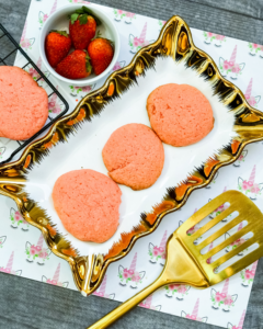 3 strawberry cake mix cookies on a platter next to a gold spatula and a bowl of strawberries