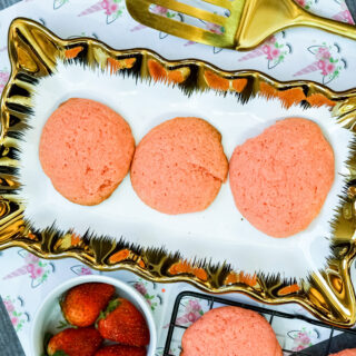 3 strawberry cake mix cookies on a platter next to a gold spatula and a bowl of strawberries