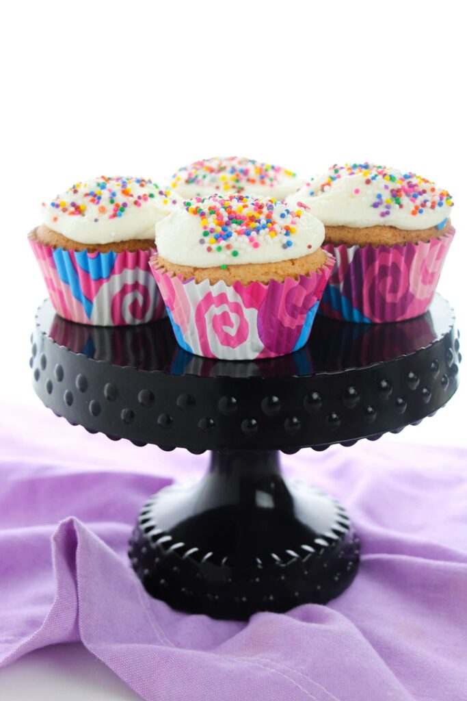 Cream Soda Cupcakes topped with sprinkles on a cake stand
