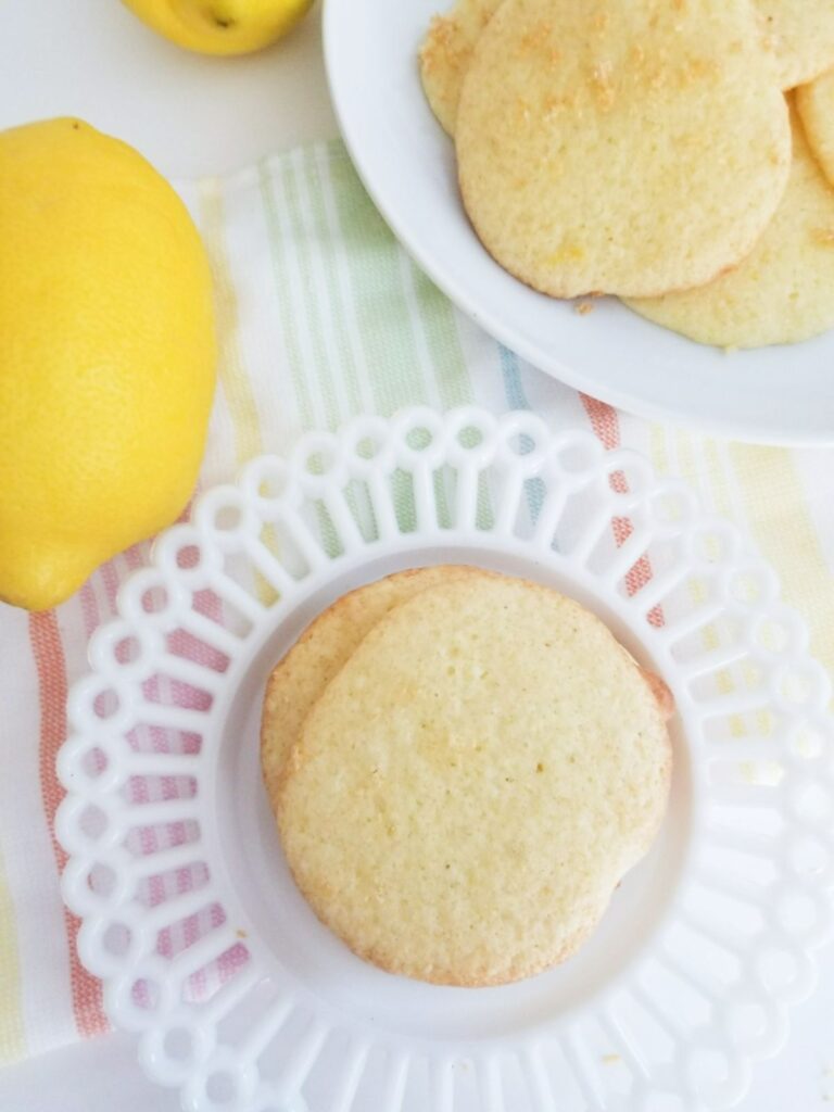 overhead view of a stack of lemon cookies from cake mix on a white plate next to more cookies on a plate and a lemon
