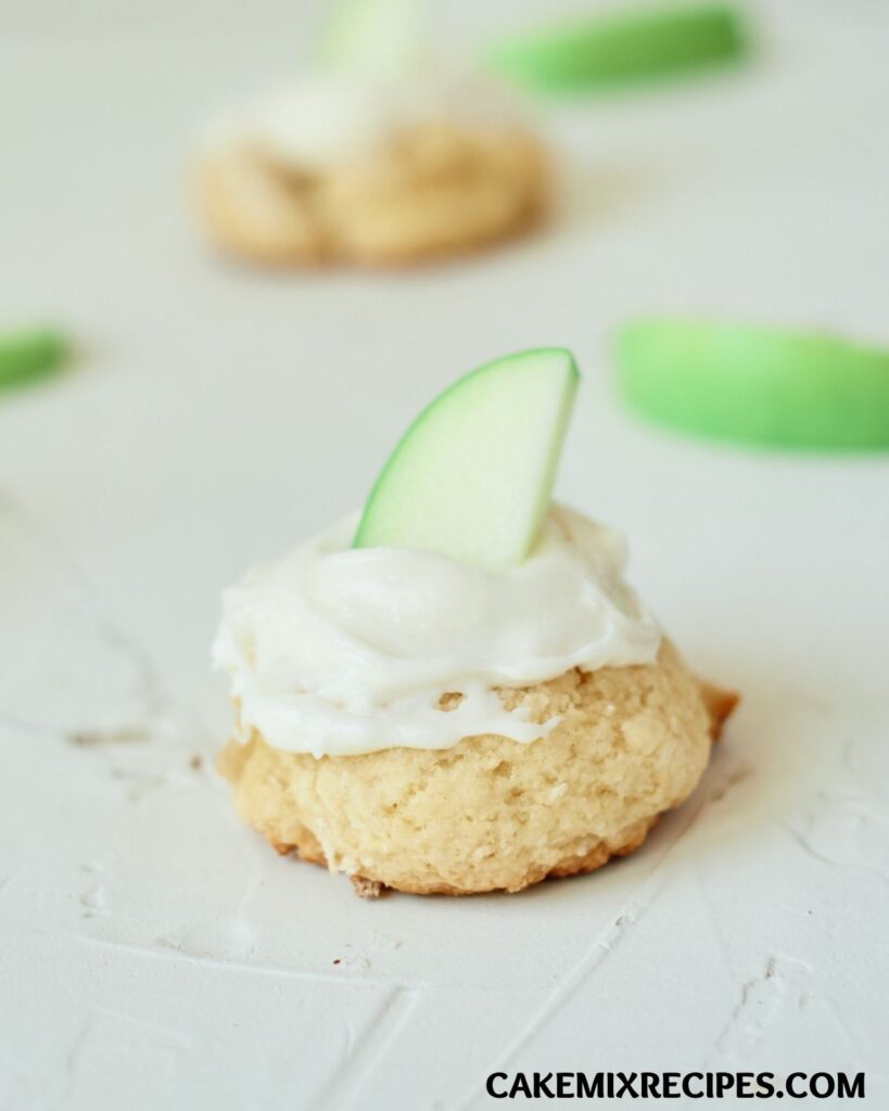 a closeup of an apple pie cookie with more cookies and slices of apple blurred in the background
