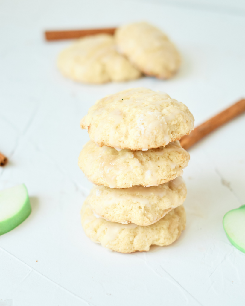 Stacked Cinnamon Apple Cookies with slices of green apple and cinnamon sticks in the background.