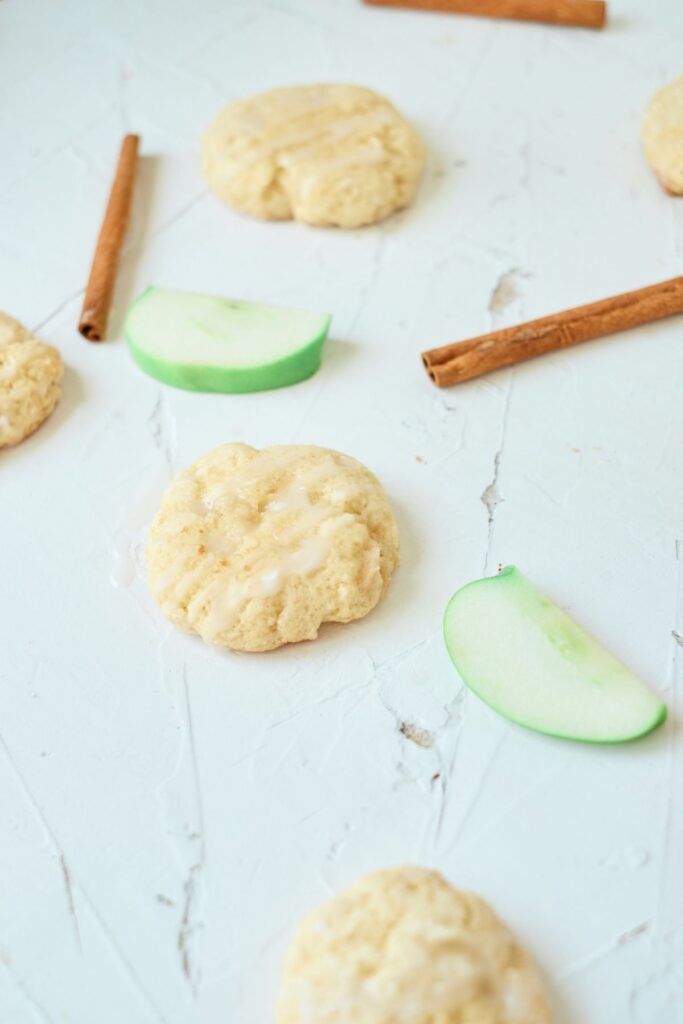 Cookies made from an apple cookies recipe with slices of green apple and cinnamon sticks in the background.
