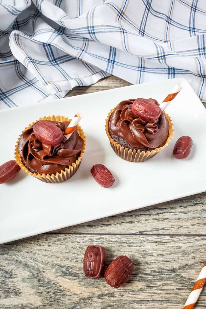 Two chocolate root beer cupcakes on a white tray with root beer barrels on the side.