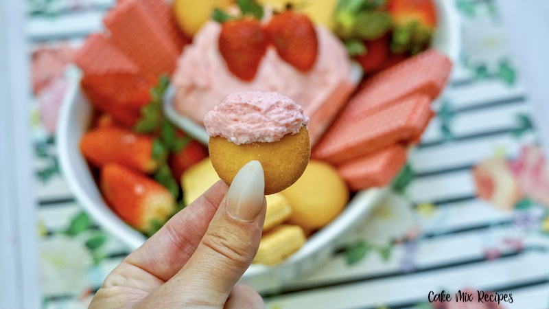 A cookie dipped in the strawberry cake batter dip ready to eat. 