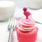 A strawberry and cream cupcake on a white plate with a fork on the side.