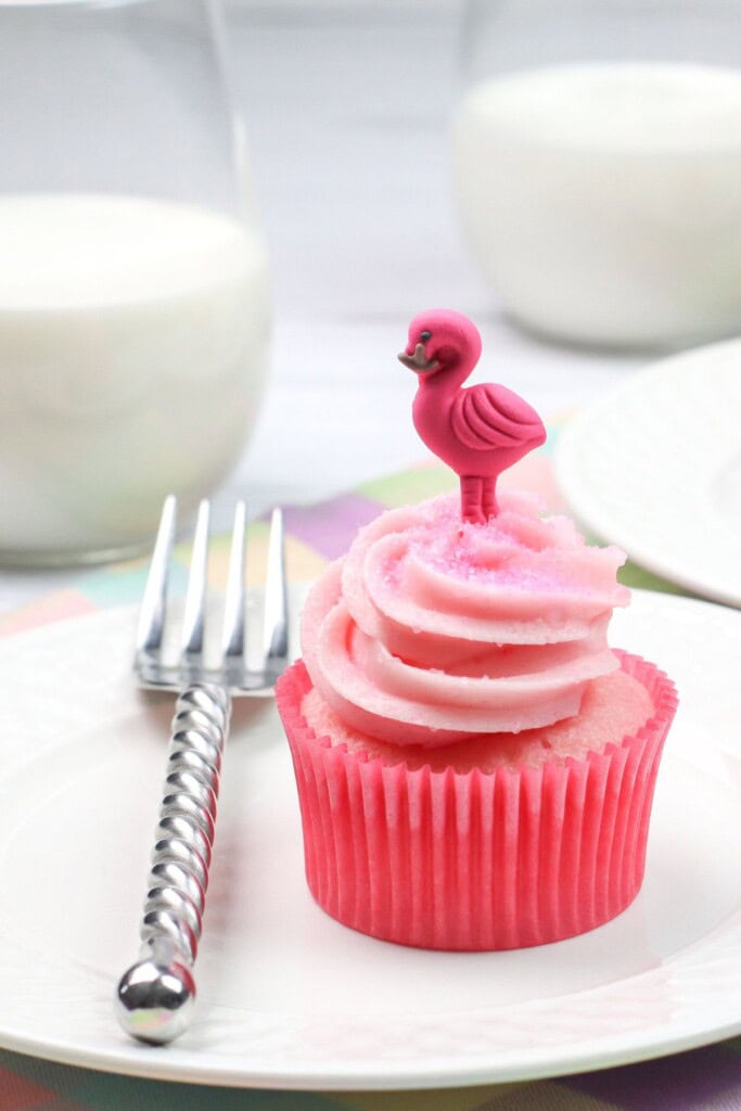 A strawberries and cream cupcake on a white plate with a fork on the side.