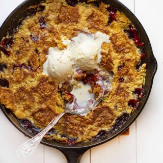 cherry dump cake in a skillet with vanilla ice cream on top