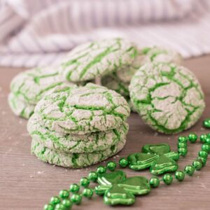 a stack of green vanilla crinkle cookies next to a green necklace and a striped cloth
