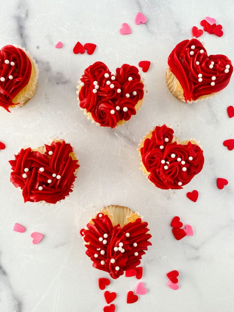 6 heart cupcakes arranged in the shape of a heart with heart confetti sprinkled around them