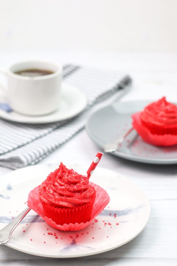 2 Shirley Temple cherry cupcakes on plates next to a cup of coffee on a cloth