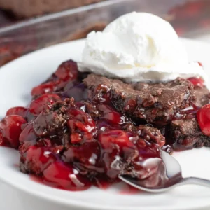 chocolate cherry dump cake on a plate with a spoon and vanilla ice cream