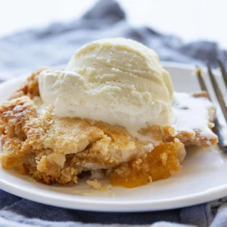 peach dump cake served on a plate with a fork and topped with vanilla ice cream