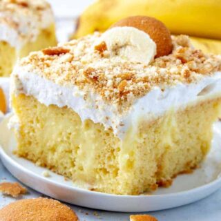 banana pudding poke cake topped with frosting, banana slices, and nilla wafers