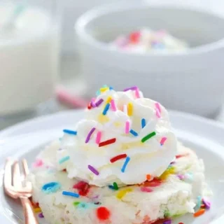 gluten free funfetti mug cake served on a plate with whipped cream and rainbow sprinkles
