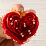A hand holding up a heart shaped cupcake.