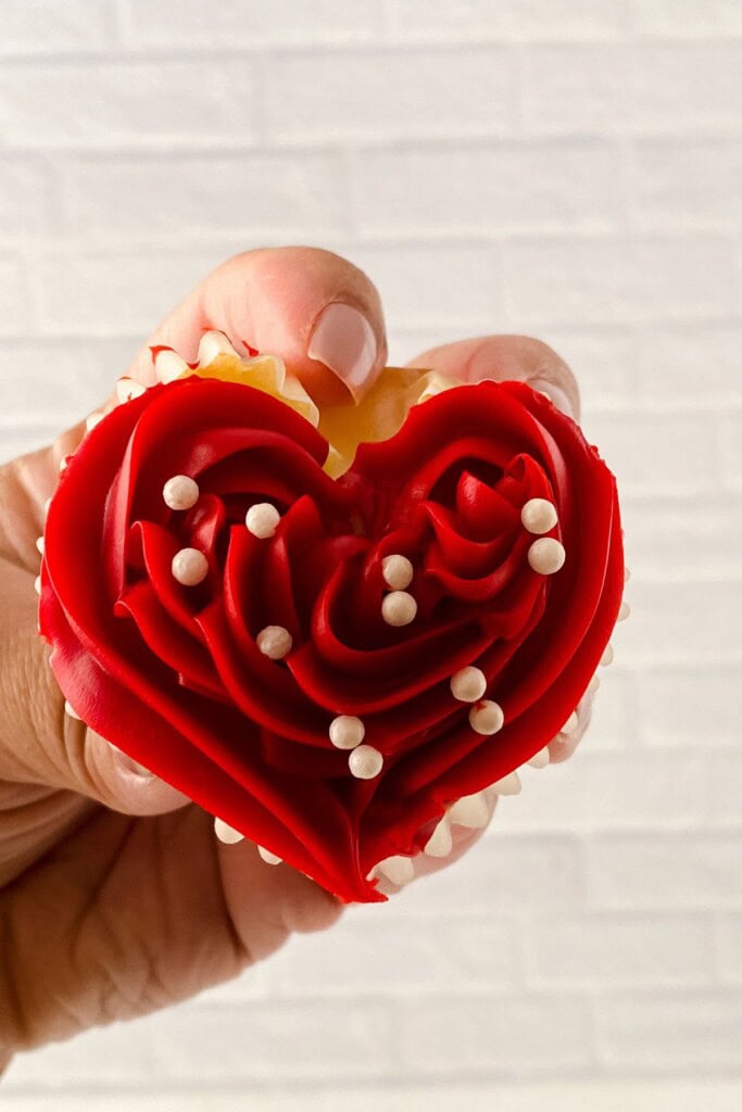 A hand holding up a heart shaped cupcake.