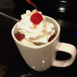 a mug cake topped with whipped cream and a cherry