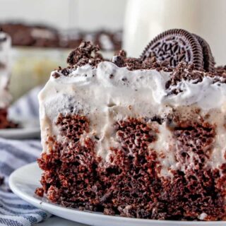 oreo poke cake served on a plate and topped with frosting and a whole oreo cookie
