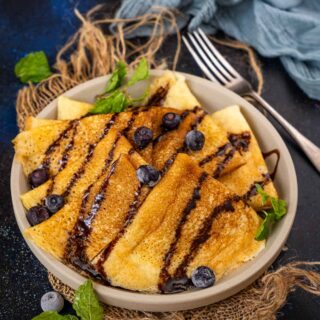 pancake mix crepes in a bowl with chocolate drizzle and blueberries