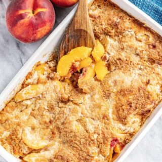 peach dump cake in a white pan with wooden serving spoon