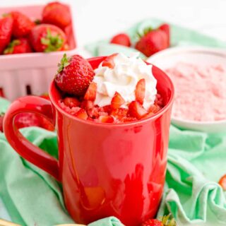 strawberry mug cake topped with a fresh strawberry and whipped cream