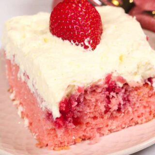 strawberry poke cake topped with vanilla frosting and whole fresh strawberry