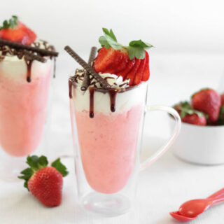 strawberry mug cake topped with whipped cream, chocolate, and fresh strawberries