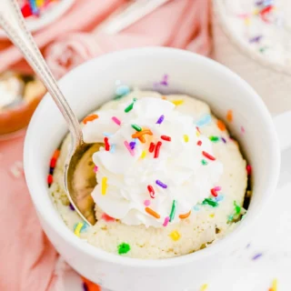 funfetti mug cake topped with whipped cream and rainbow sprinkles