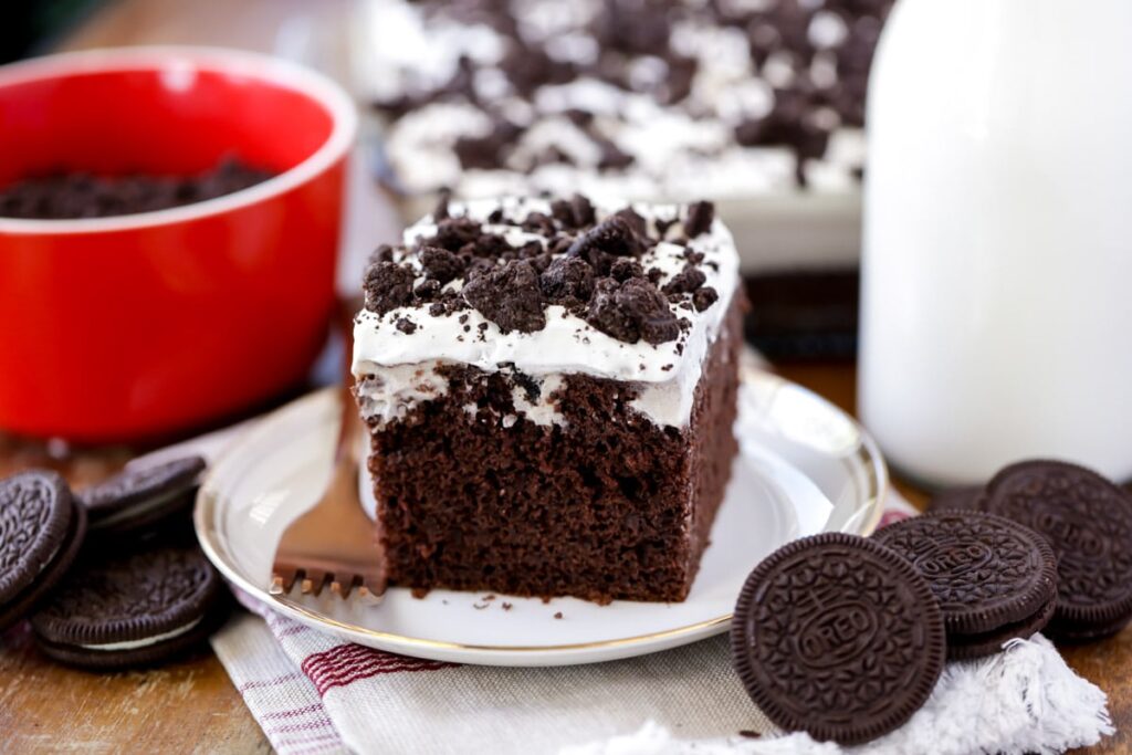 oreo pudding poke cake served on a white plate with three oreos on the side