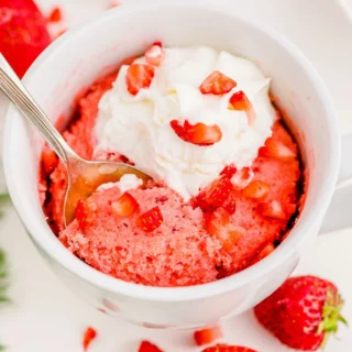 strawberry mug cake topped with whipped cream and fresh strawberry pieces