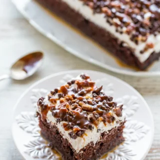 turtle chocolate poke cake topped with frosting, caramel, and assorted nuts