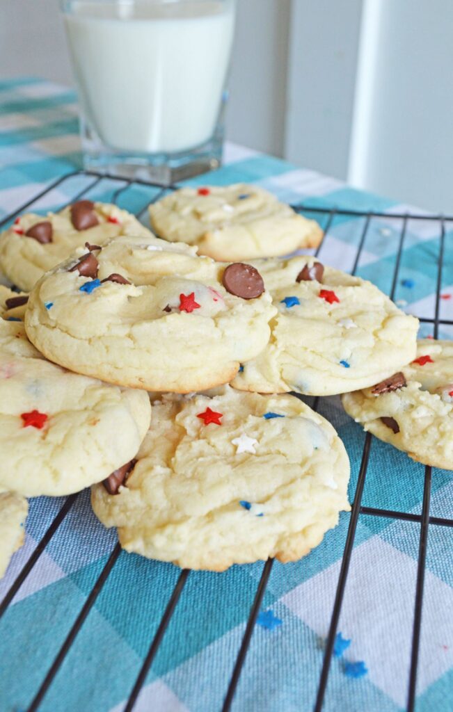 a stack of Chocolate Chip Cake Mix Cookies on a wire rack on a blue cloth next to a glass of milk