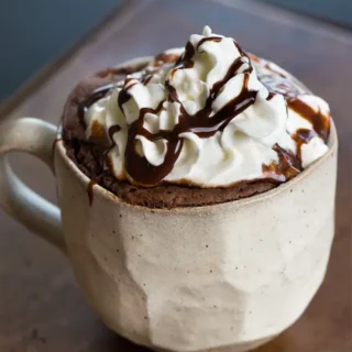 chocolate protein cake in a mug topped with whipped cream and chocolate syrup
