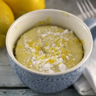 lemon mug cake served in a dish and topped with powdered sugar and lemon zest