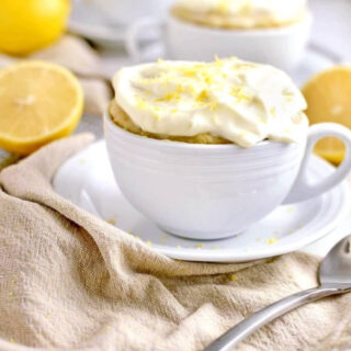 lemon cake in a mug topped with frosting and lemon zest