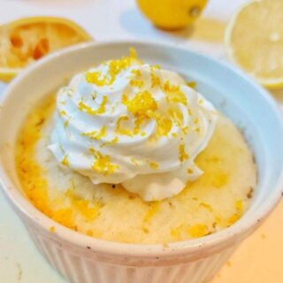 lemon cake in a mug topped with whipped frosting and lemon zest