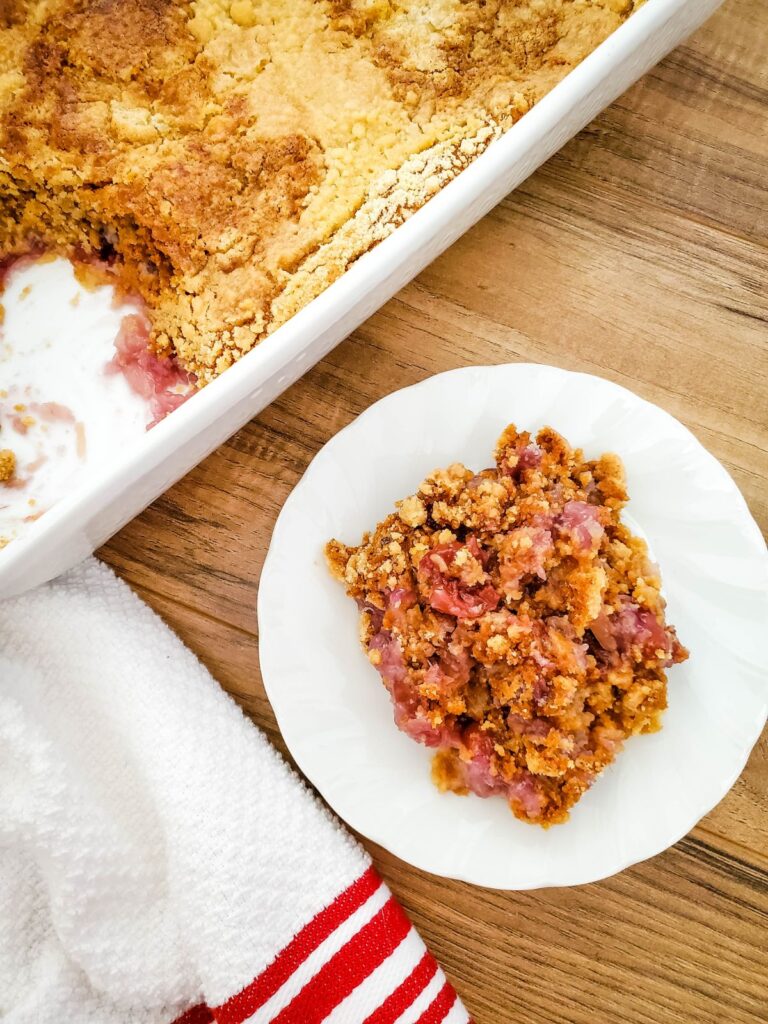 pineapple dump cake with cherries on a white plate on a brown table with more cake in a dish in the background