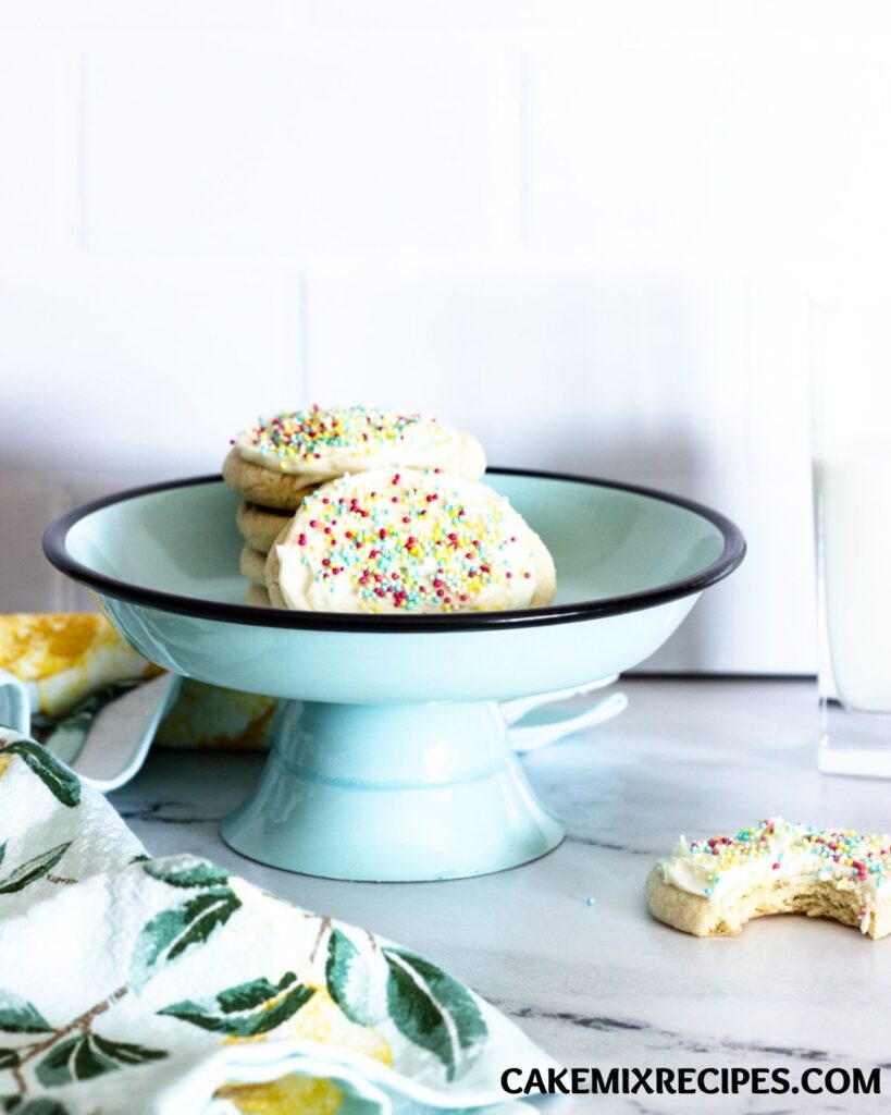 sugar cookies with cake mix stacked on a light green cake plate next to a cloth and a cookie with a bite taken out of it