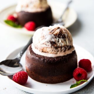 chocolate lava cake served in a plate topped with ice cream and a side of raspberries