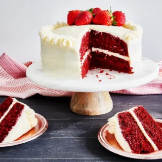 a full red velvet cake from mix cut into with two slices on the table that are topped with frosting and strawberries