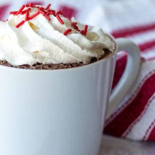vanilla mug cake in a white mug with cool whip and red sprinkles on top