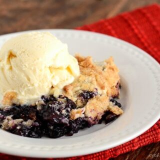 Blueberry Pineapple Dump Cake with vanilla ice cream on top, in a shallow white bowl