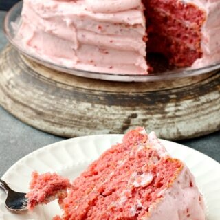 Strawberry cake with pink frosting on white plate with fork on the side