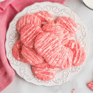 Strawberry Cake mix cookies on a white plate with drizzled white frosting on top
