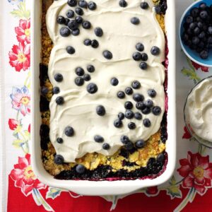 Glass Casserole dish filled with lemon blueberry dump cake, with icing and fresh blueberries ontop