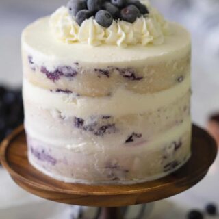 Lemon Blueberry cake with white icing and blueberries on top, on a wooden stand