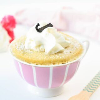 Keto vanilla mug cake in a pink tea cup with cool whip and a vanilla bean on top