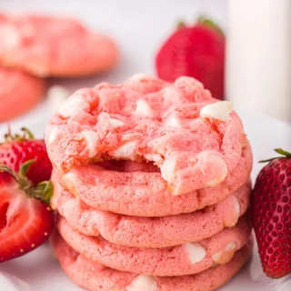 Strawberry cake mix cookies with white chocolate chips stacked on top of one another with fresh strawberries on the sides