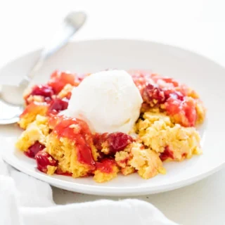 Fruity Dump Cake with vanilla ice cream on top in a shallow white bowl with a spoon on the side